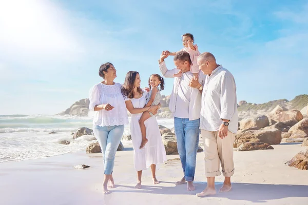 A smiling mixed race three generation family with little girls walking together on a beach. Adorable little kids bonding with mother, father, grandmother and grandfather outside.