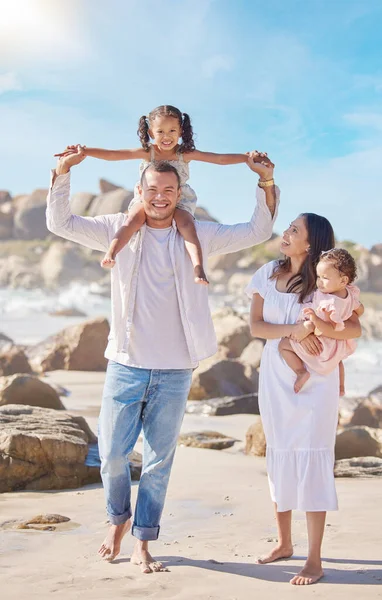 A happy mixed race family of four enjoying fresh air at the beach. Hispanic couple bonding with their daughters while walking and carrying their daughters.