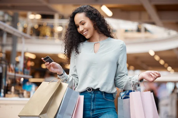 One beautiful mixed race woman holding a credit card and standing in a mall shopping. Young hispanic woman carrying bags, spending money, looking for sales and getting in some good retail therapy.