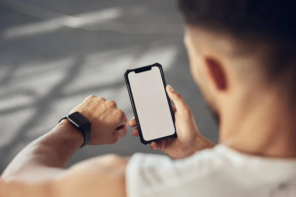 Athlete using their smartphone to track their progress. Fit man using a watch to track workout progress. Athlete using an online app to connect with their watch and cellphone in the gym.