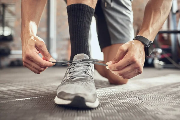 Fit athlete tying his shoe laces. Closeup on the hands of an athlete getting ready to workout. Closeup on the sport shoe of a bodybuilder. Athlete tying shoe laces cropped.