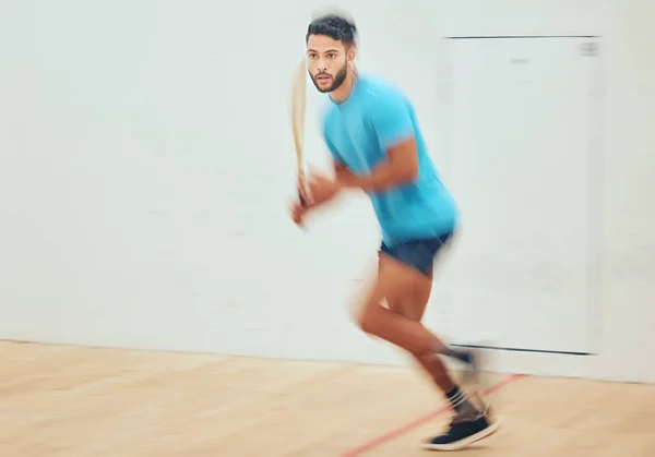Young athletic squash player running while playing court game with copyspace and motion blur. Fit mixed race athlete moving with speed during training practice in sports centre. Sporty hispanic man.