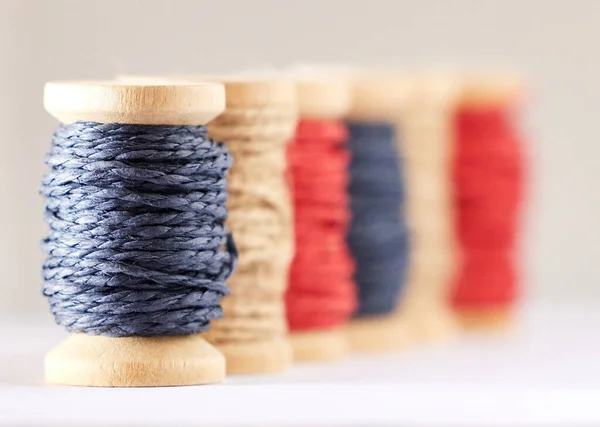 Many rolls of coloured yarn or string lined up in a row in studio isolated against a grey background. For the production of textiles, sewing, crocheting, knitting, weaving, embroidery or rope making.