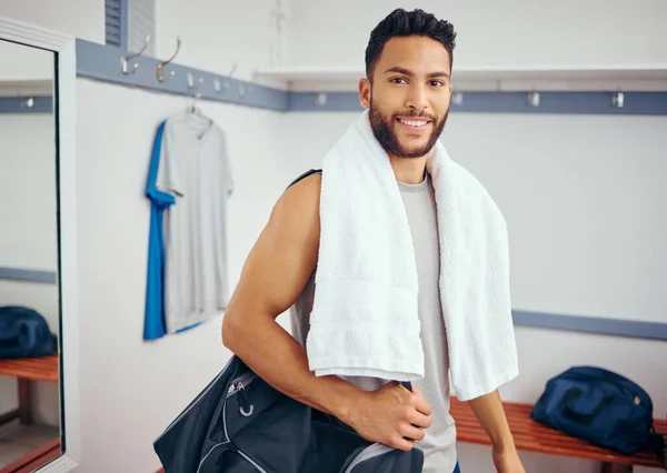 Portrait of a happy player in his gym locker room. Mixed race man ready for a squash match. Young man relaxing in his gym after a game. Young man carrying his gym bag through his locker room.