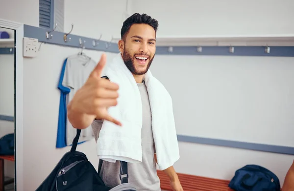 Cheerful man making a hand gesture in his gym locker room. Portrait of a mixed race man taking a break from his match to relax in his gym locker room. Happy athlete relaxing after a squash match.