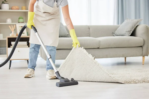 An unknown domestic worker lifting and cleaning under a carpet. One mixed race unrecognizable female using a vacuum cleaner under a mat to begin spring cleaning.