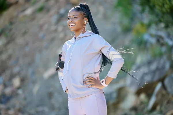 Young happy african american woman hiking on a mountain, taking a break to rest. Black ethnic fit smiling young woman working out in nature. Athletic woman standing on a hiking trail relaxing while