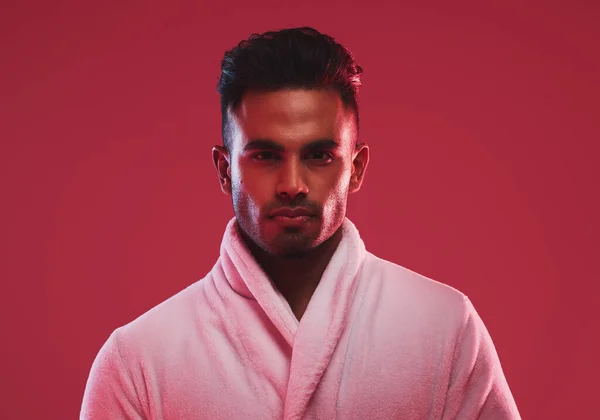 Athletic young male model wearing a bathrobe while posing posing against a red background. Handsome young hispanic man posing in the studio.