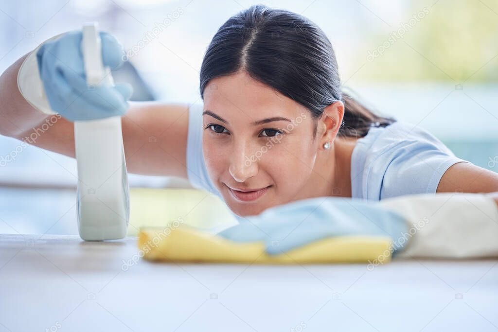 One beautiful smiling young mixed race woman cleaning the surfaces of her home. Happy Hispanic domestic worker wiping a table.