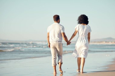 Sahilde birlikte yürürken el ele tutuşan melez genç bir çift. İspanyol çift tatilin tadını çıkarıyor ve sahilde romantik oluyor..
