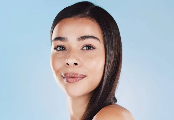 Portrait of one beautiful young hispanic woman with healthy skin and sleek hair posing against a blue studio background. Mixed race model with flawless complexion and natural beauty.