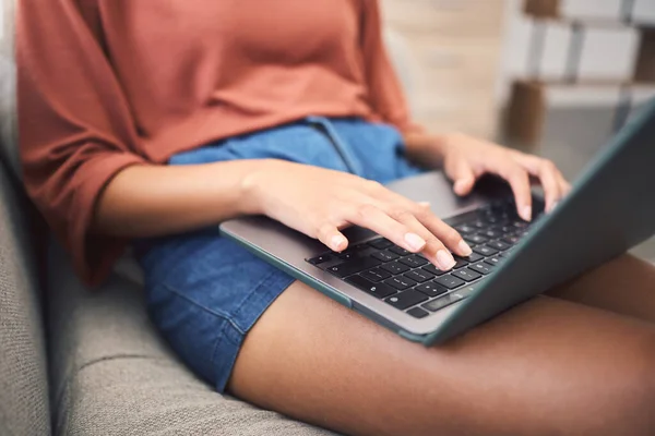 Closeup shot of an unrecognizable mixed race woman using a laptop while doing remote work from the couch. Young female doing freelance work while using the internet for research and sending an email.