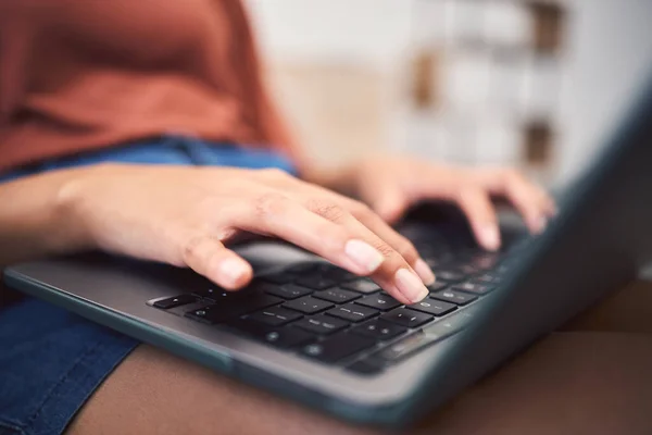Closeup shot of an unrecognizable mixed race woman using a laptop while doing remote work from the couch. Young female doing freelance work while using the internet for research and sending an email.