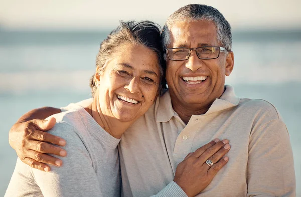 Closeup portrait of an senior affectionate mixed race couple standing on the beach and smiling during sunset outdoors. Hispanic couple showing love and affection on a romantic date at the beach.