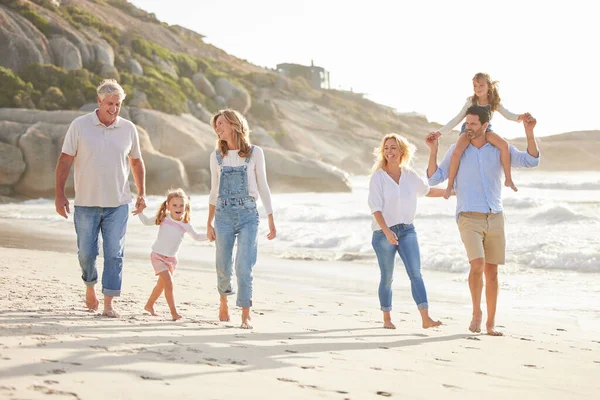Multi generation family holding hands and walking along the beach together. Caucasian family with two children, two parents and grandparents enjoying summer vacation.