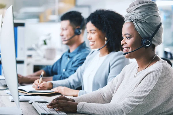 African american female call centre telemarketing agent working on computer alongside colleagues in an office. Group of diverse consultants troubleshooting solution for customer service and sales