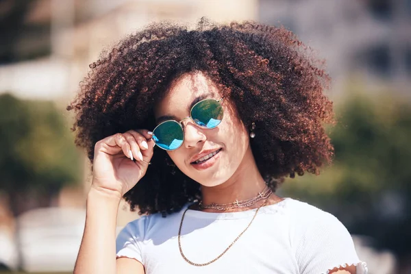 Cool, happy hispanic woman wearing sunglasses outside. Cheerful young woman with a curly afro wearing trendy, stylish sunglasses while enjoying a summer day at the park outside. Young woman smiling.