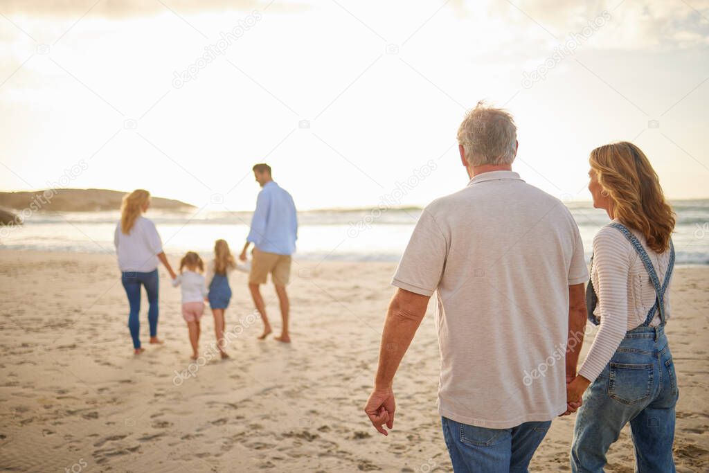 Rear view of Multi generation family holding hands and walking along the beach together. Caucasian family with two children, two parents and grandparents enjoying summer vacation.