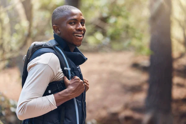 One young handsome african american male backpacker hiking outdoors in the woods. Confident and happy black man walking through the forest, sightseeing and enjoying his favourite weekend activity.