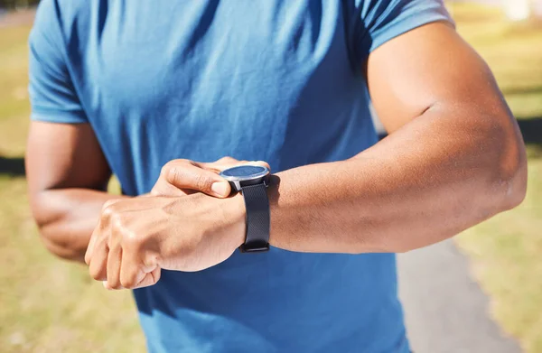 Closeup of unknown fit active mixed race man using a smartwatch to time a workout and check his heart rate after training outdoors alone. Muscular hispanic athlete monitoring calories during exercise.