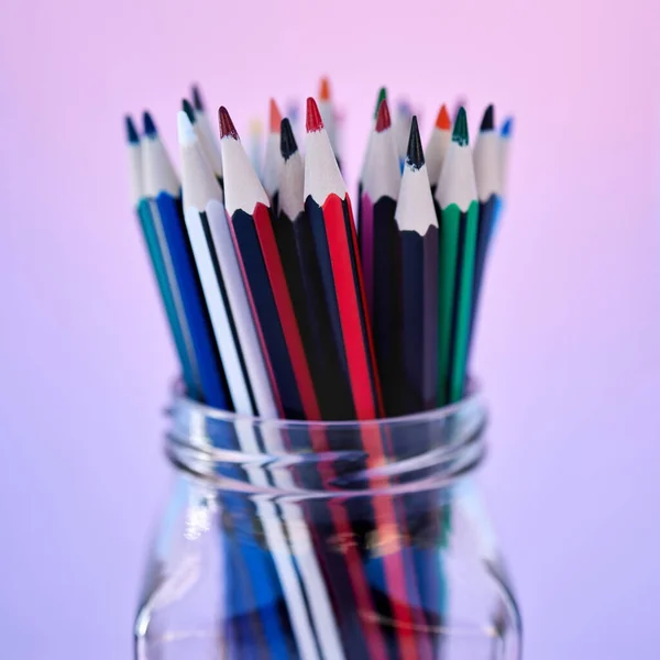 Closeup of many pencils in a glass jar isolated on a colorful background. Macro view of stationery for art and drawing. School supplies for a student or artist. Education and creative still life.