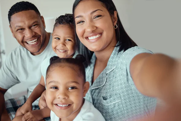 Photo of a loving mother holding phone and taking selfie or recording funny video with her family at home. Happy mixed race family with two children and parents posing together for a family picture on