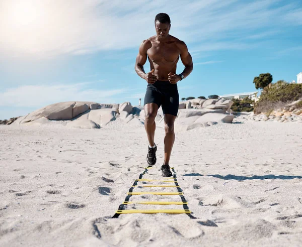晴れた日にビーチで砂の中で彼の訓練中に敏捷性はしごを使用して1つのスポーティ運動アフリカ系アメリカ人の男性 日中に軽率な運動をする男性スポーツマンにフィットします 健康のために — ストック写真