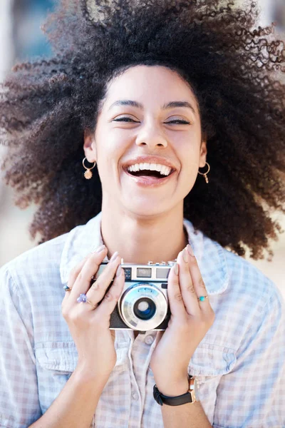 Young mixed race woman with curly hair taking creative photos on a vintage retro film camera. One female photographer looking in viewfinder while capturing pictures as a hobby or profession on a shoot