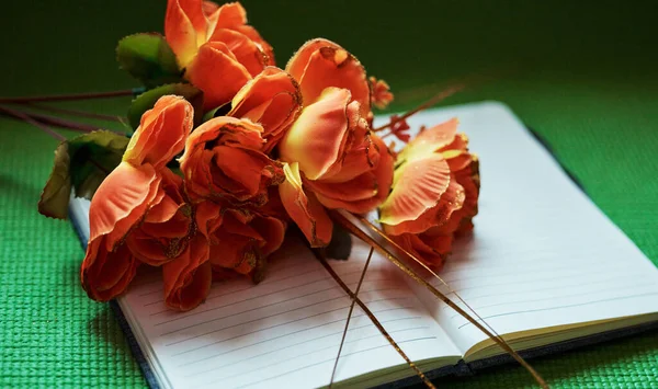 Above shot of orange flowers on an open notepad. Nature can inspire us to write and spark our creativity. Get productive and motivated in a creative environment. Write down dreams, plans and goals.