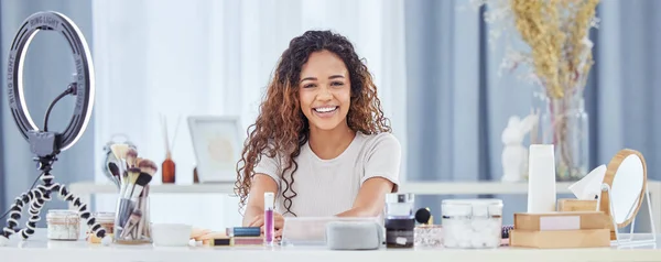 One hispanic woman recording a makeup tutorial for her beauty blog with her phone while sitting at home. African american female influencer live streaming her cosmetic review and recommendation online