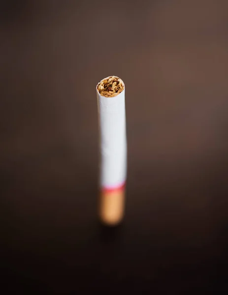Closeup of a cigarette isolated on dark background. Stop smoking and quit bad habits like tobacco. Addiction is unhealthy and causes cancer. The tobacco industry has a dark side