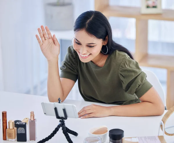 Smiling female beauty blogger waving at her smart phone while recording a video or broadcasting live. Beautiful young influencer sharing her beauty products and regime.