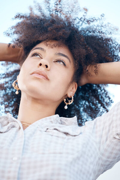 Closeup shot of a beautiful young mixed race female with her hands in her afro. Below shot of one african american woman looking thoughtful and contemplative while standing outside. Full of ideas.