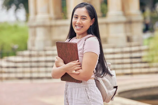 One mixed race female student standing outside on her university campus while wearing a backpack. A beautiful young woman holding her digital tablet outdoors while on break between college classes.
