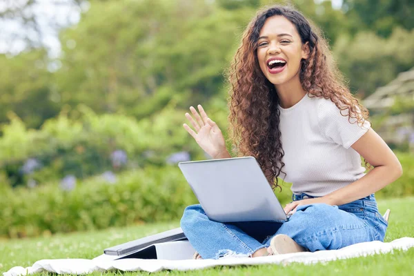 One young hispanic woman working on her laptop while sitting outside on an open field. A beautiful mixed race female student smiling while using her computer to study online on her university campus.