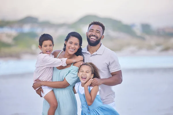 Portrait of a cheerful mixed race family laughing while standing together on the beach. Loving parents spending time with their two children during family vacation by the beach.