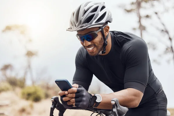 Smiling male cyclist using his smartphone while sitting on his bike. Fit sportsman smiling and using mobile phone while cycling outdoors.