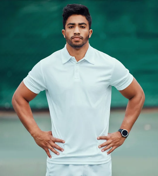 Portrait of serious indian tennis player standing alone on a court. Fit ethnic sports professional with hands on hips and feeling confident in a sports club. Ready for an athletic and healthy game.