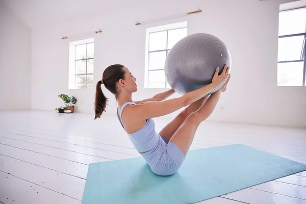Strong woman training her core with a ball. Young woman using exercise ball in yoga studio. Dedicated using exercise ball to balance. Fit woman exercise her abs in pilates class.