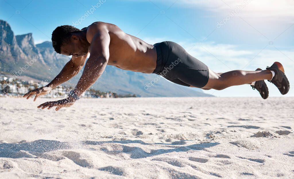 Fit young black man doing plank hold exercises on sand at the beach in the morning. African American muscular male bodybuilder athlete doing bodyweight workout to build a strong core and endurance.