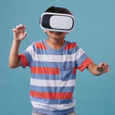 Genç melez çocuk ayakta ve kablosuz bir VR kulaklık takıyor ve mavi arka planda bir video oyunu oynuyor. Eğlence ve oyunlar hafta sonu içindir..