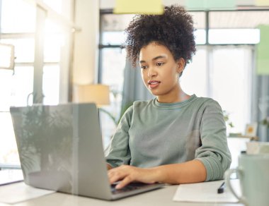 Genç melez bir kadın dizüstü bilgisayarda çalışıyor evde bir masada oturuyor. Odaklanmış, kıvırcık saçlı bir kadın evdeki lobide tek başına e-posta yazıyor..