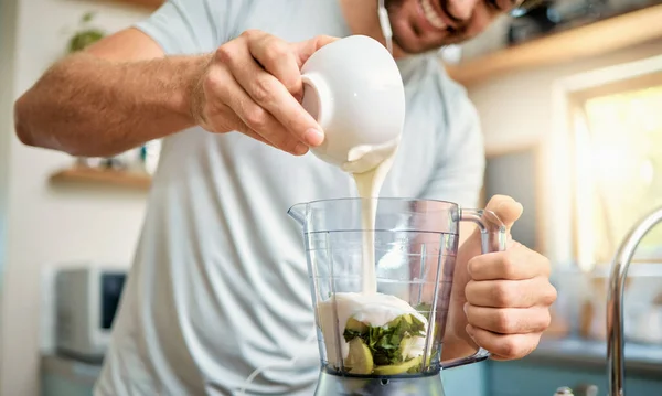 Closeup of one caucasian man pouring yoghurt into blender for healthy green detox smoothie in kitchen at home. Guy having fresh fruit juice to cleanse and provide energy for training. Wholesome drink