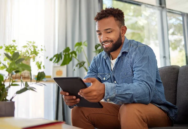 Handsome bachelor reading on his digital tablet. Happy bachelor enjoying his day at home relaxing. Always connected to the online world with his wireless tablet. Young man resting on his couch.