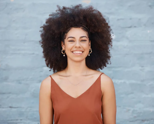 Portrait of cheerful woman with big afro and beautiful smile standing outside against a brick wall. Carefree woman posing outside during the day.