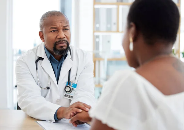 Serious gp in a consult with a patient. African american doctor talking to a patient in a checkup. Woman getting support from her doctor during a checkup. Doctor holding a patients hand.