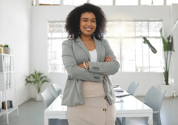 Young happy mixed race businesswoman standing with her arms crossed while in an office alone. One confident hispanic female boss with a curly afro smiling and standing at work.