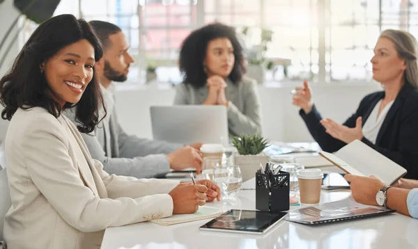 Portrait of a young african american businesswoman sitting in a meeting at work. Group of businesspeople having a meeting together at a table. Business professionals talking and planning in an office.
