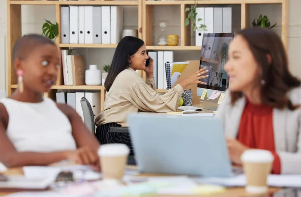 Serious ambitious indian business woman using cellphone to talk to clients while using office computer. Confident ethnic professional sitting behind team, explaining and sharing ideas while networking