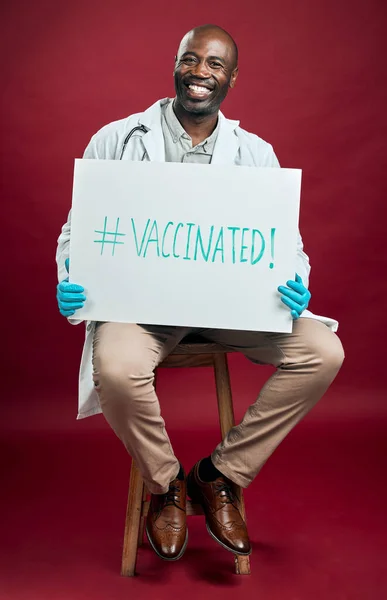アフリカ系アメリカ人のCovid医師がポスターを掲載しています コピースペースと赤いスタジオの背景に対して隔離された笑顔の黒い医師の完全な長さの肖像画 サインでコロナワクチンを推進する男 — ストック写真